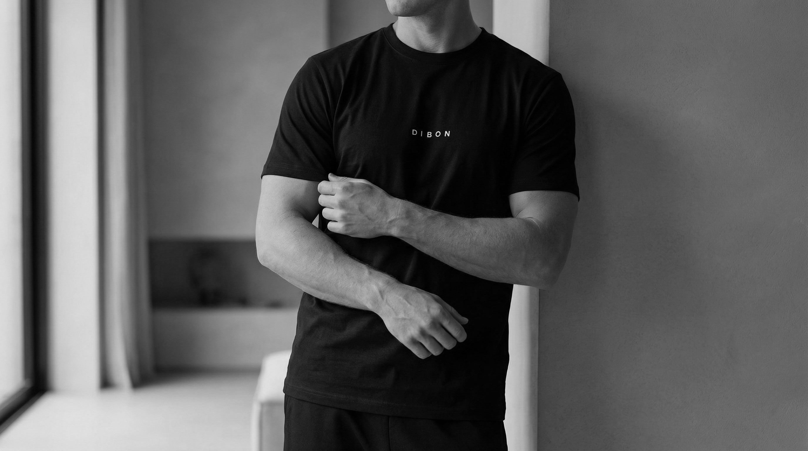 Person wearing a black t-shirt with a logo in a minimal indoor 